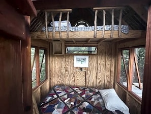 A wooden cabin interior with a bed, windows, and a quilt. - Texas Safari Camp Hummingbird Tree House (Kaufman)