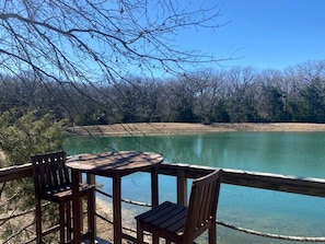 Terraza de madera con mesa y sillas con vista a un lago tranquilo.