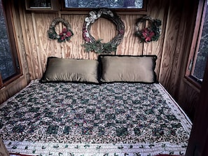 Ein Zimmer mit Holzwänden, einem Bett, zwei Kissen und drei Weihnachtskränzen an der Wand.