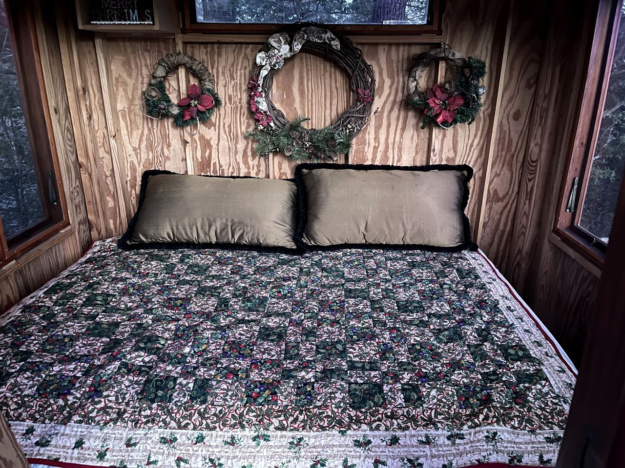 Ein Zimmer mit Holzwänden, einem Bett, zwei Kissen und drei Weihnachtskränzen an der Wand.