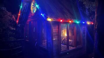 A small, illuminated wooden cabin with a large window, a door, and a chimney.