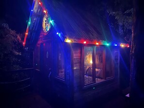 Eine kleine, beleuchtete Holzhütte mit großem Fenster, Tür und Schornstein.