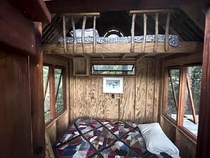 A wooden cabin interior with a bed, windows, and a quilt.