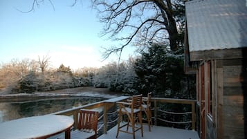 A wooden deck with a table and chairs, overlooking a body of water and trees.