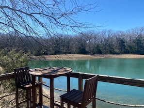 A wooden deck with a table and chairs overlooking a calm lake. - Texas Safari Camp Hummingbird Tree House (Kaufman)