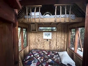 Interior de una cabaña de madera con cama, ventanas y colcha.