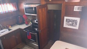 A compact kitchen with a microwave, oven, and sink. There is a door leading to another room and a small window with curtains. - Hatteras Sleeps 8 & SelfDrive 20' Pontoon Fishing Lobstering Snorkeling Sandbar (Key West)