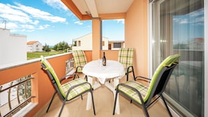 Un balcon avec une table et des chaises, une bouteille, et une vue sur le quartier.