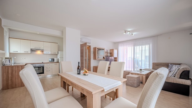 Une cuisine moderne dotée d’appareils électroménagers intégrés, un coin repas avec une table et des chaises en bois, et un salon avec un canapé et un téléviseur.
