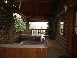 Eine Holzterrasse mit Whirlpool, einer überdachten Sitzgelegenheit und Blick ins Freie.