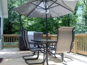 Eine Terrasse im Freien mit Tisch, Stühlen, Sonnenschirm und Grill.