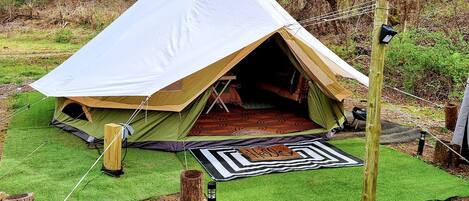 Una carpa con una entrada amplia, rodeada de césped artificial verde, un tapete estampado y un poste de madera.