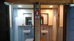 A bathroom with two sinks, a shower, and a toilet. There is a wooden bench and a sign indicating a baby changing area.