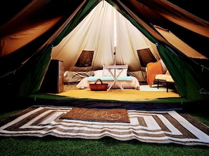 A tent with a bed, a small table, and a welcome mat.