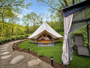 A tent with a bed inside, surrounded by a garden with a stone path and chairs.