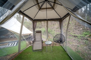 A tent with a cushioned chair and a small table, surrounded by green artificial grass.