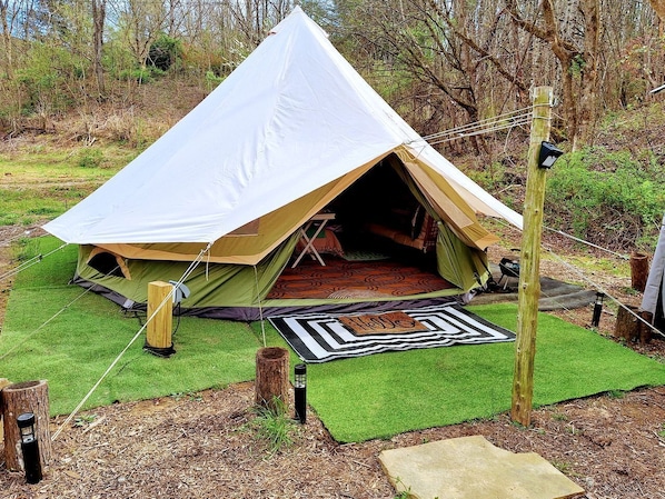 A tent with a large entrance, surrounded by green artificial grass, a patterned mat, and a wooden post.
