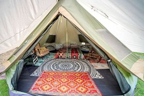 A tent with a circular bed, two chairs, and a patterned rug.