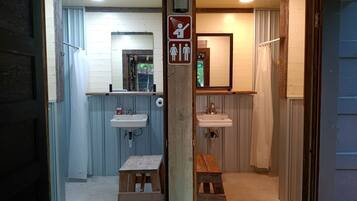 A bathroom with two sinks, a shower, and a toilet. There is a wooden bench and a sign indicating a baby changing area.