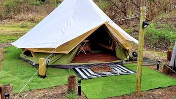 A tent with a large entrance, surrounded by green artificial grass, a patterned mat, and a wooden post.