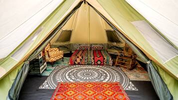 A tent with a circular patterned rug, two beds with colorful bedding, and a small wooden chair.