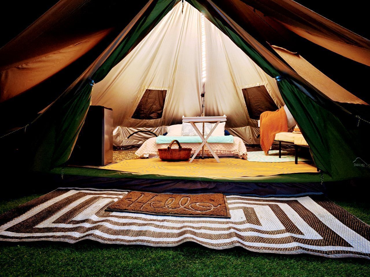A tent with a bed, a small table, and a welcome mat.