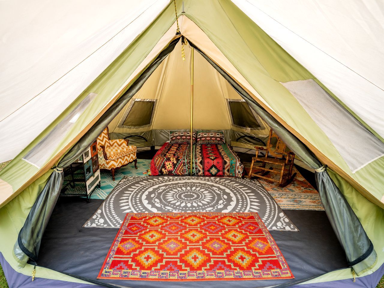 A tent with a circular patterned rug, two beds with colorful bedding, and a small wooden chair.