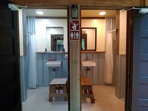 A bathroom with two sinks, a shower, and a toilet. There is a wooden bench and a sign indicating a baby changing area.