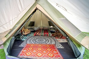 A tent with a circular bed, two chairs, and a patterned rug.