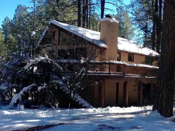 A cabin with a chimney, wooden deck, and snow-covered surroundings.