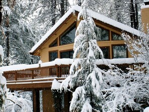 A wooden cabin with a balcony, surrounded by snow-covered trees.