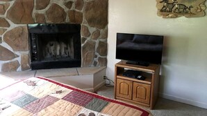 Una chimenea de piedra, un televisor sobre un soporte de madera y un colcha en el suelo.