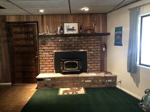 A room with a brick fireplace, a wooden door, a green rug, and a window with curtains. - Cabin Getaway near to Pine, Arizona that is Perfect for a Family Vacation (Pine)
