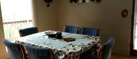 A dining room with a table set for four, blue upholstered chairs, a floral tablecloth, and a decorative wall shelf.