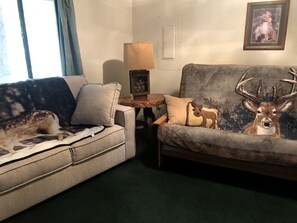 A living room with a sofa, a small table with a lamp, and a deer-themed wall decoration.
