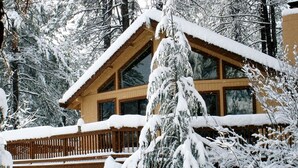 Una cabaña de madera con balcón, rodeada de árboles cubiertos de nieve.