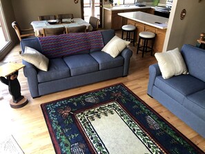 A living room with a blue sofa, a patterned rug, a dining table, and a kitchen area.