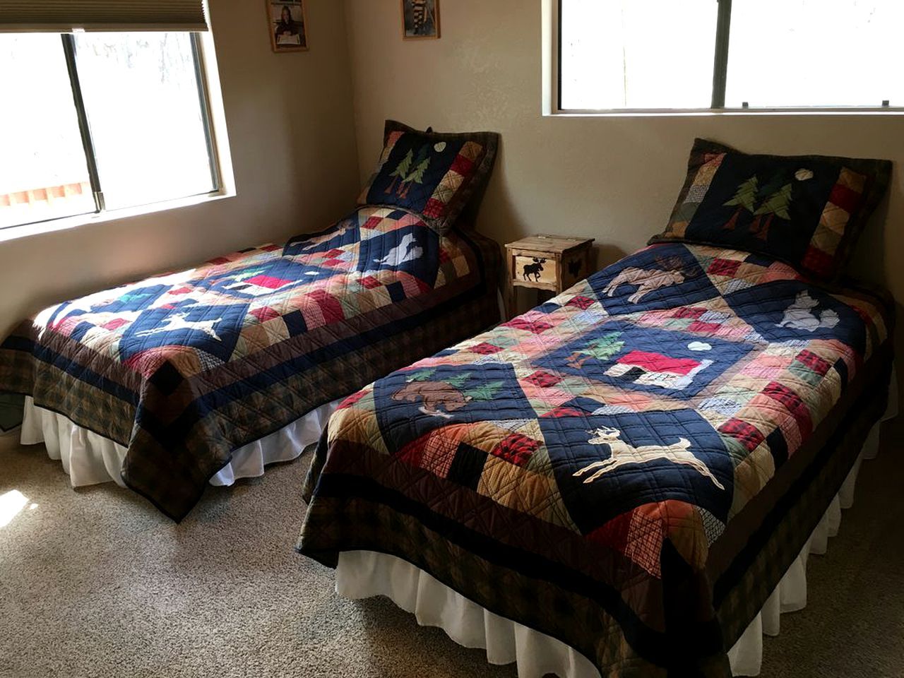 Deux lits jumeaux avec des couvertures matelassées, une fenêtre et une petite table de chevet en bois.