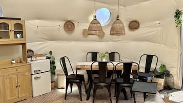 Un espace repas aménagé sous une tente, avec une table, des chaises, des lampes suspendues et un buffet.