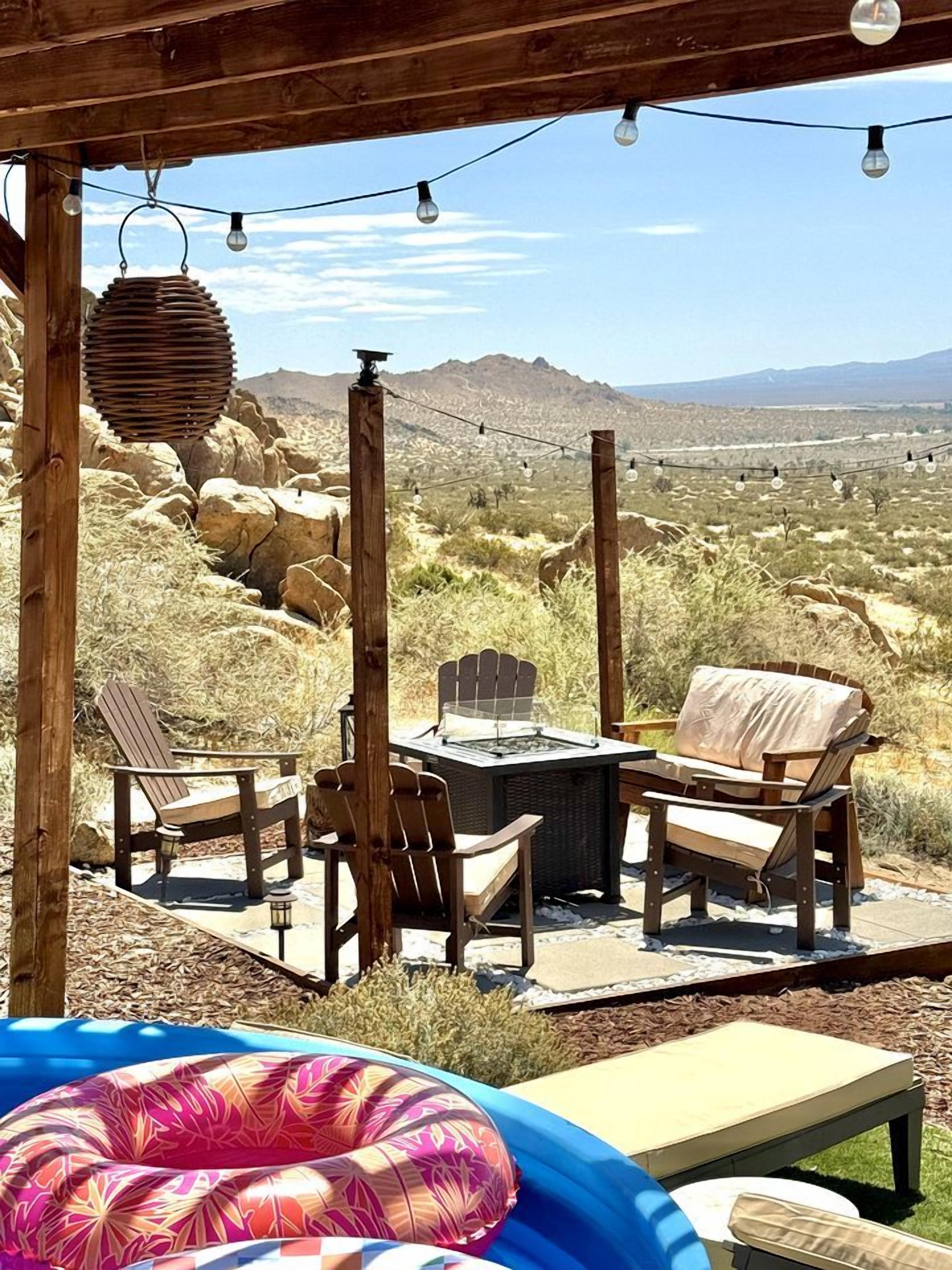 An outdoor patio with wooden furniture, a grill, and a view of a desert landscape.