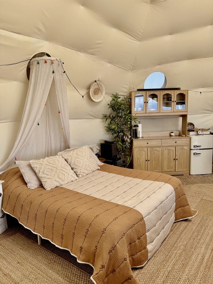 Una camera da letto con un letto a baldacchino, un angolo cottura e uno specchio rotondo al muro.