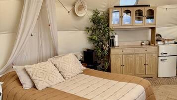 A bedroom with a canopy bed, a small kitchenette, and a round mirror on the wall.