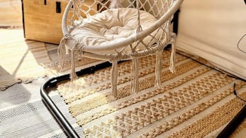 Un fauteuil suspendu à l’intérieur d’une structure en forme de tente, offrant une vue sur l’extérieur.