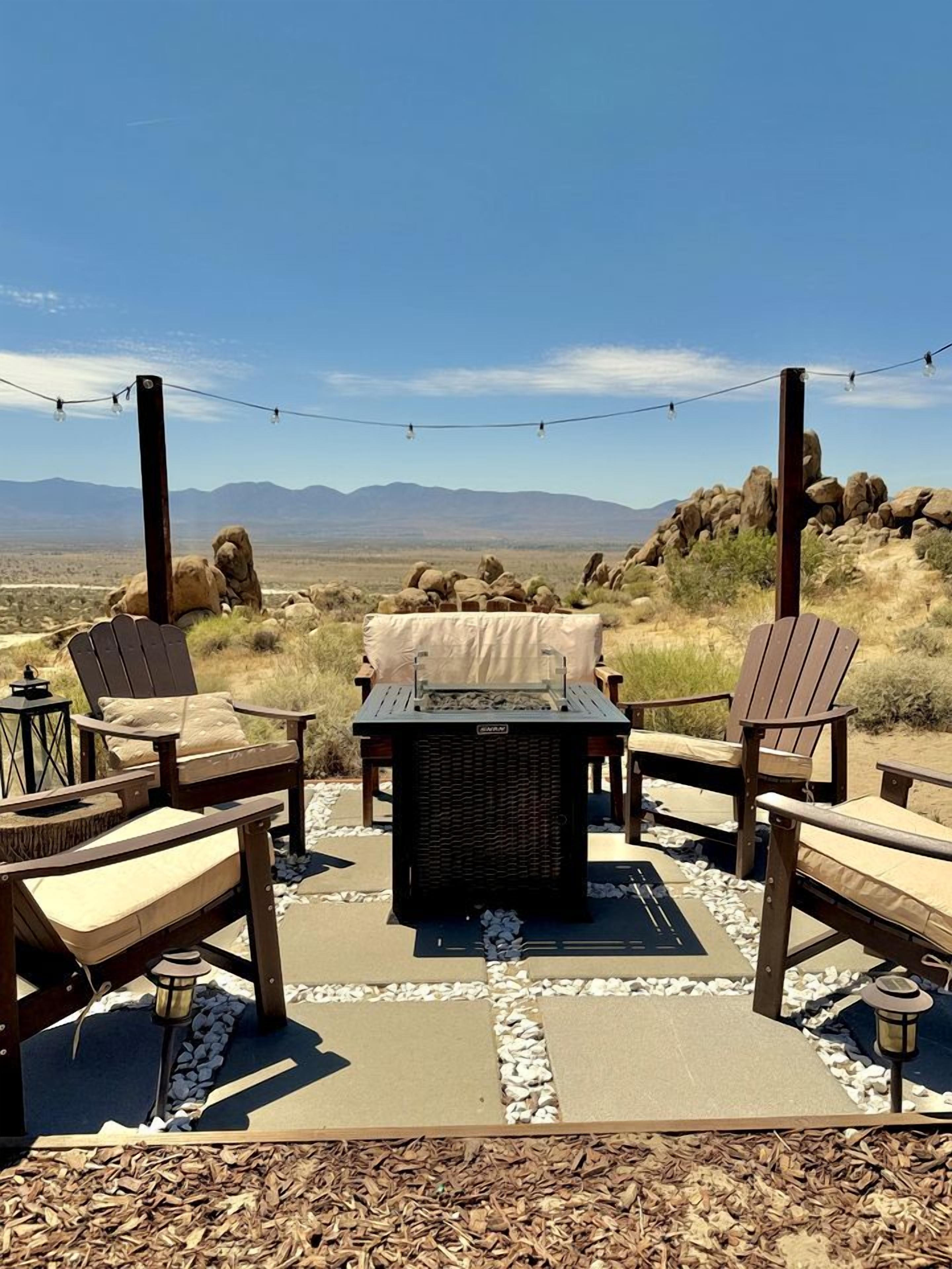 An outdoor seating area with Adirondack chairs, a fire pit, and string lights.