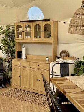 A tented room with a wooden cabinet, a table, chairs, and a hanging light fixture.