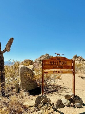 A wooden sign with 'The Hilltop' and 'EST. 2021' visible, set in a desert landscape with rocks and sparse vegetation.