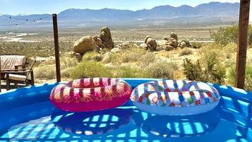 An outdoor pool with two inflatable rings, a wooden deck, and a view of mountains in the background.