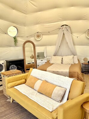 A cozy bedroom with a canopy bed, a sofa, a small table, a mirror, and a fireplace.