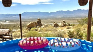 An outdoor pool with two inflatable rings, a wooden deck, and a view of mountains in the background. - Stunning Geo Dome with Joshua Tree vibes (Palmdale)