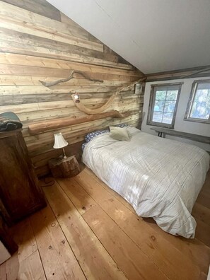 A bedroom with a wooden wall, a bed, a nightstand, a lamp, and a window.